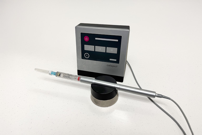 Computer Assisted Local Anesthesia machine. Calaject dental anesthesia system featuring a digital control unit with labeled buttons (I, II, III, R), a connected handpiece with syringe attachment, and a cylindrical stand for support.